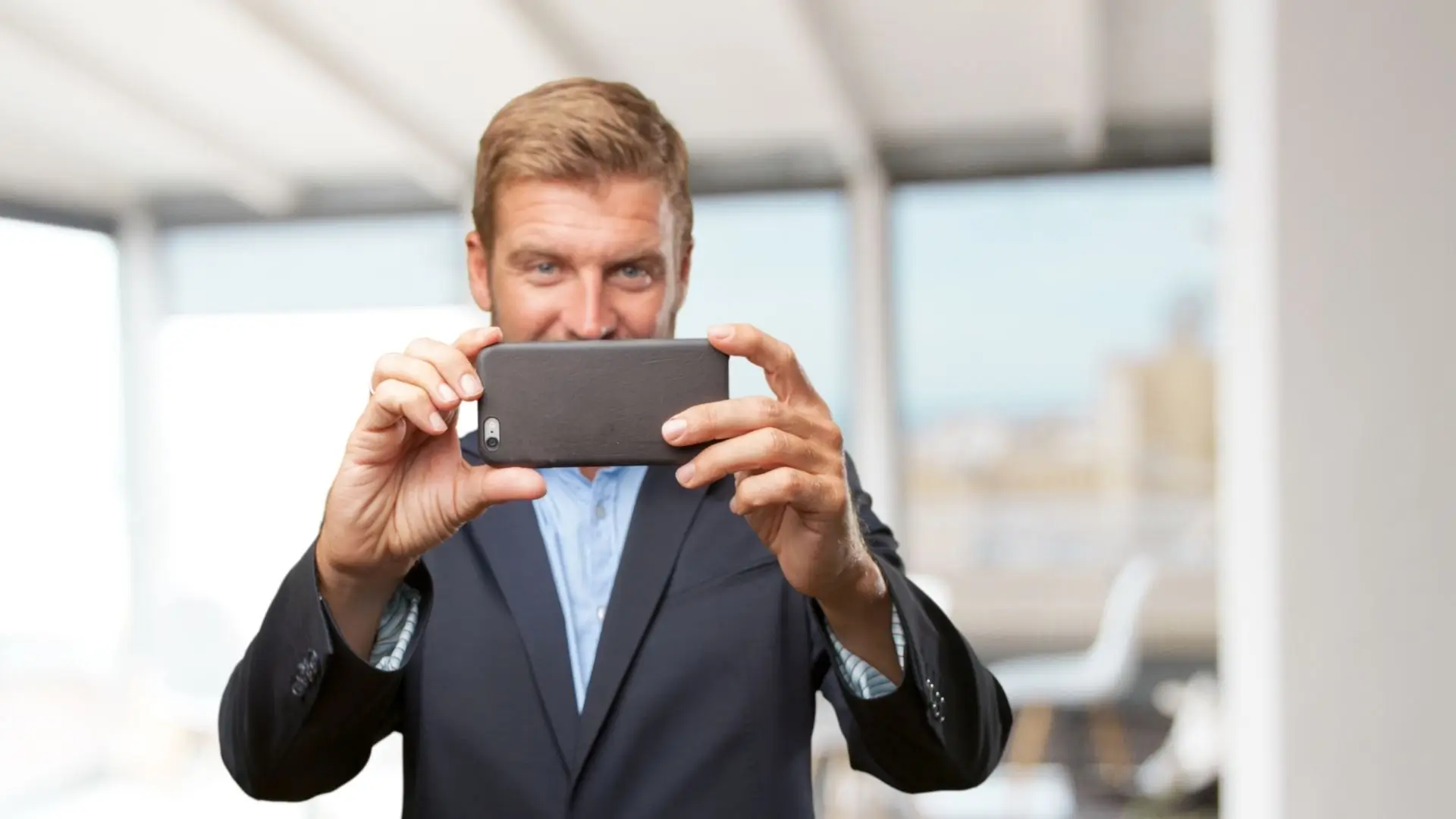 A man in a suit captures a moment with his phone, showcasing a blend of professionalism and modern technology.