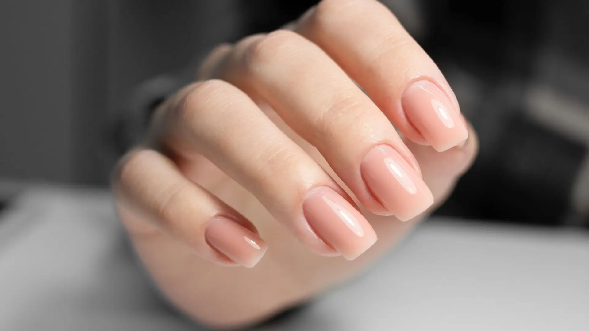 A close-up of a woman's hand with pink nails against a clean white background, showcasing elegance and simplicity.