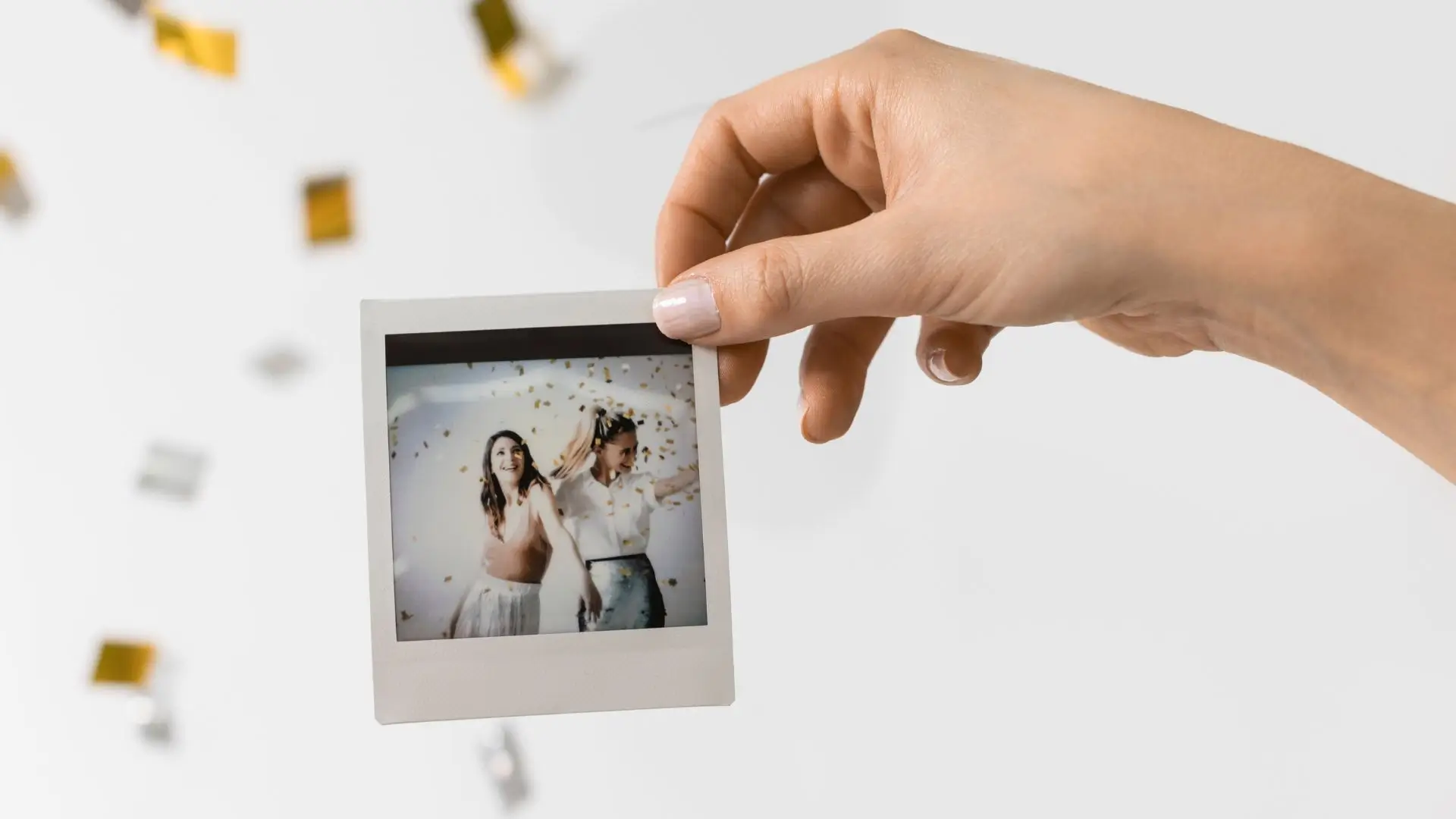A person holds a polaroid photo as colorful confetti cascades down from the sky, creating a festive atmosphere.