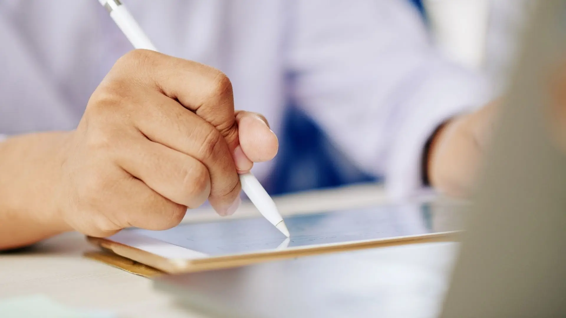 A person writes on a tablet with a pen, focused on their task in a well-lit environment.