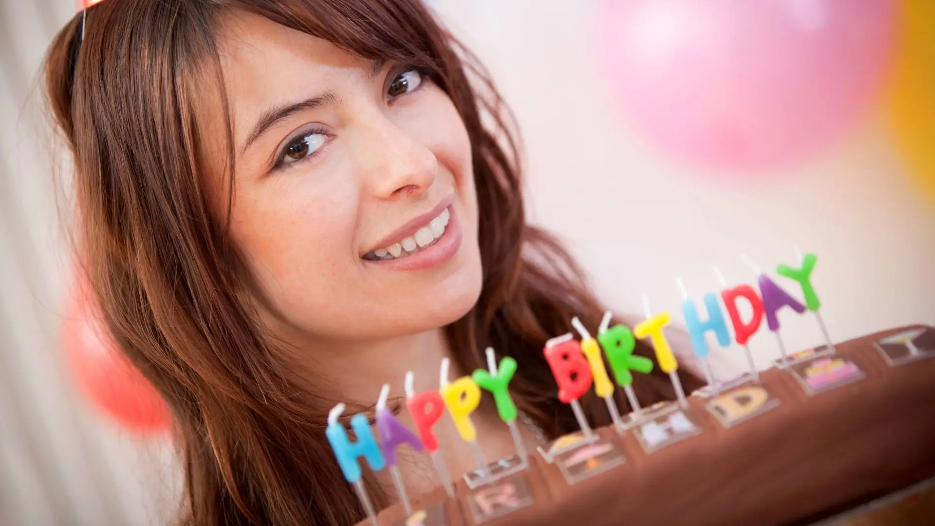 A woman smiles while holding a birthday cake adorned with lit candles, celebrating a special occasion.