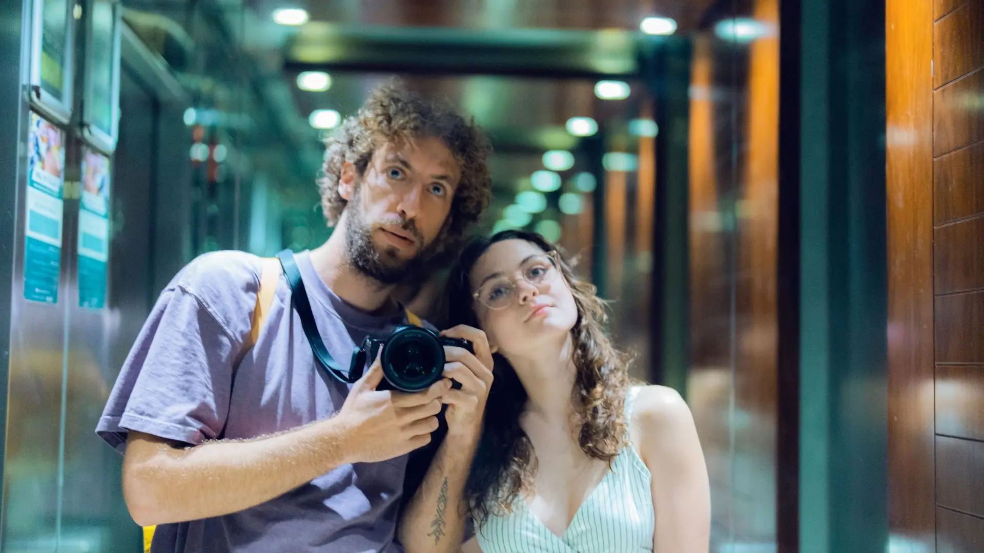 A man and woman smiling together while taking a photo with a camera outdoors.