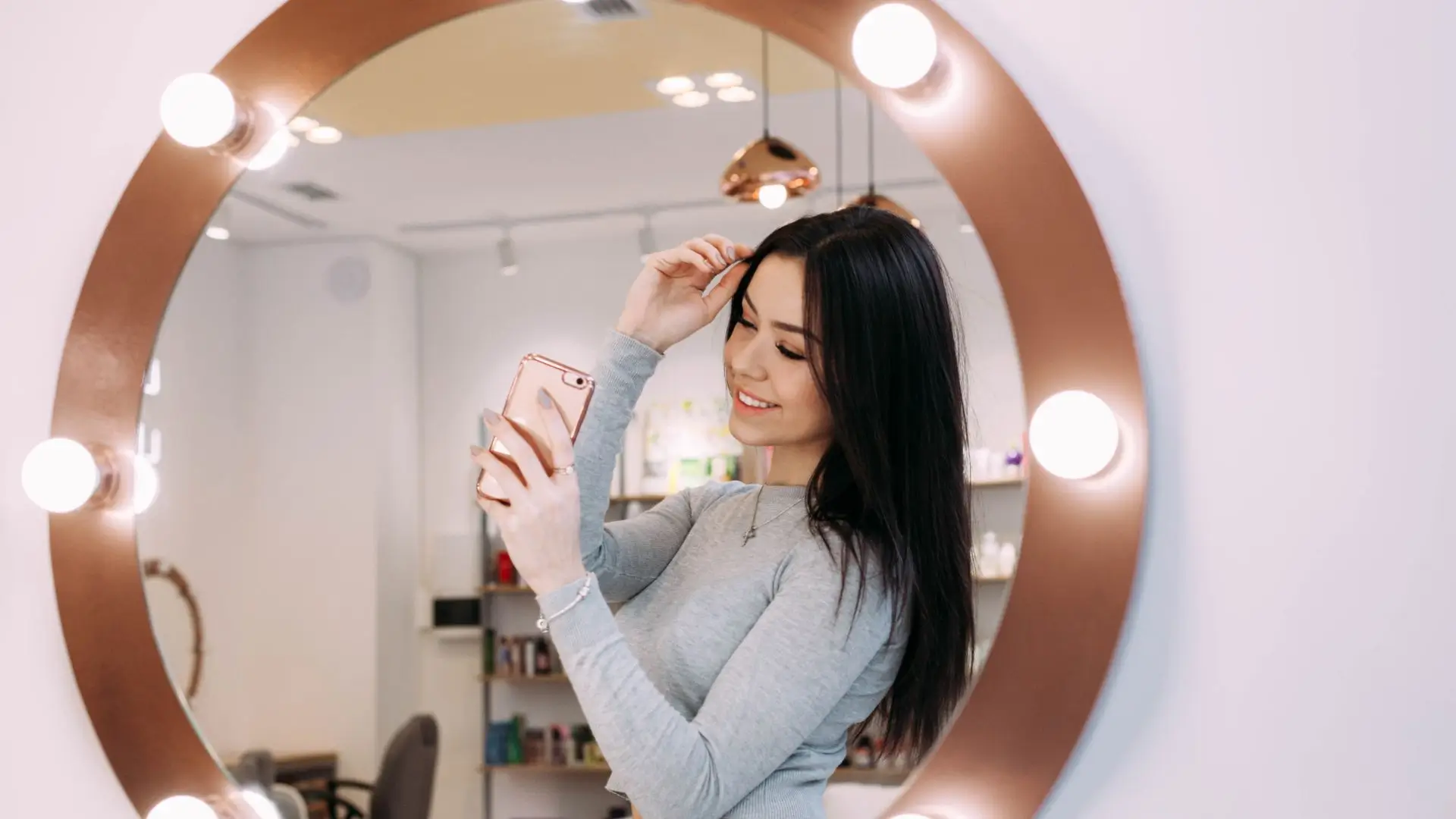 A woman gazes at her phone reflected in a mirror, capturing a moment of contemplation and connection.