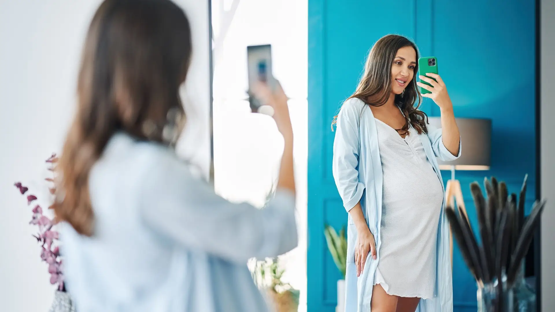 A woman in a robe smiles as she takes a selfie in front of a mirror, capturing a moment of self-expression.