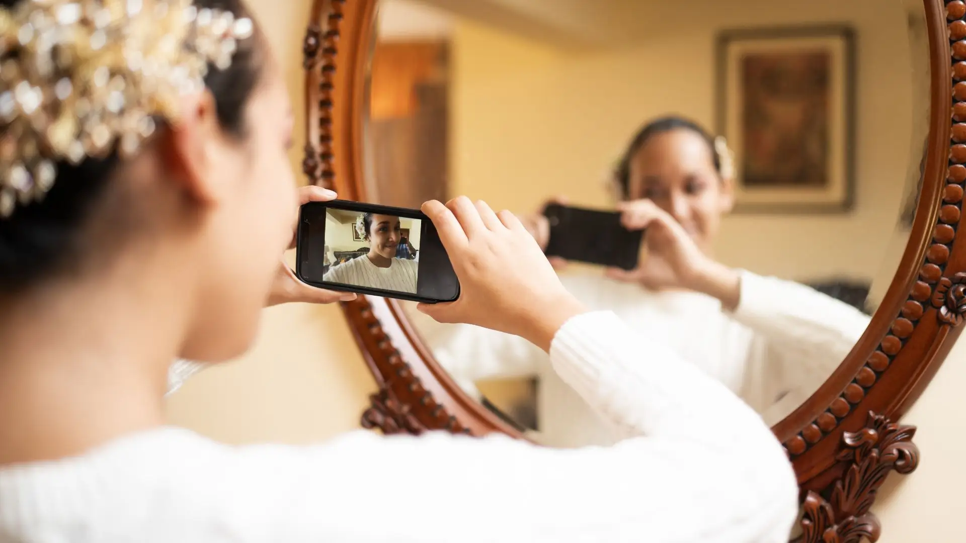  A woman capturing a selfie in the mirror, smiling and showcasing her outfit with confidence.