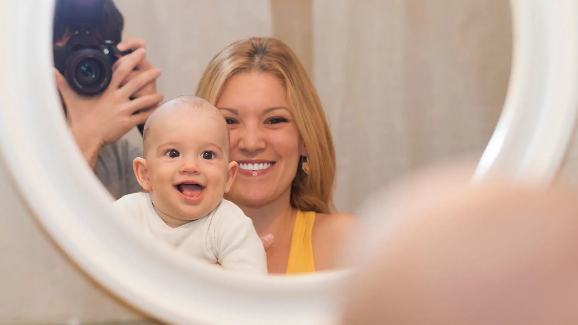 A woman lovingly holds a baby in front of a mirror, reflecting their bond and shared moment of tenderness.