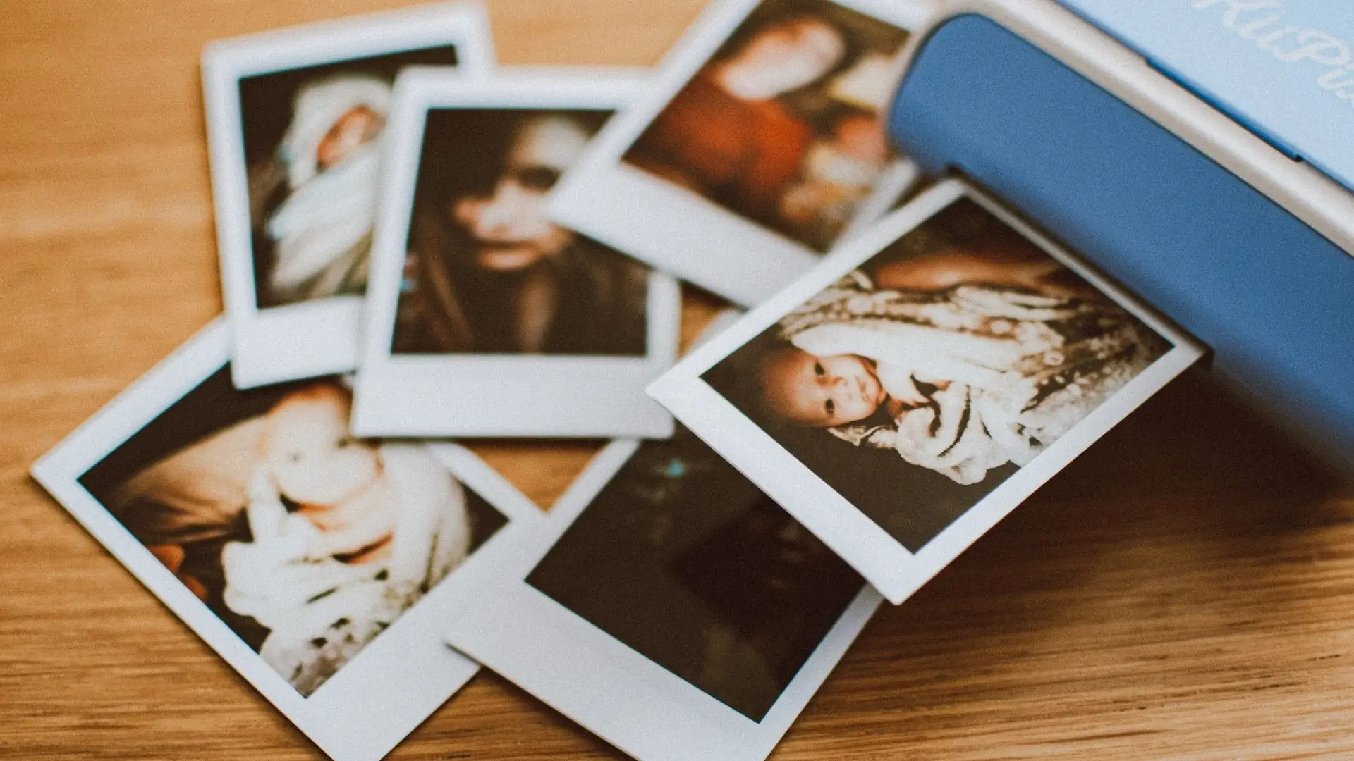 A blue Polaroid printer surrounded by several printed photos, showcasing vibrant memories captured in an instant.