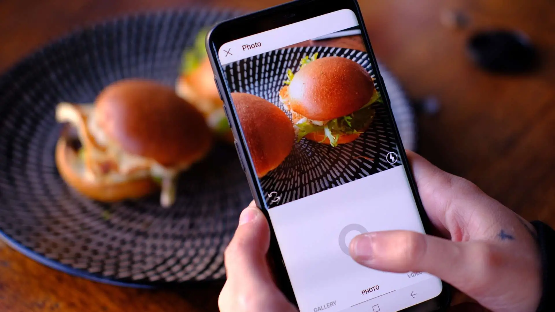 A person capturing a photo of a plate featuring two delicious hamburgers.