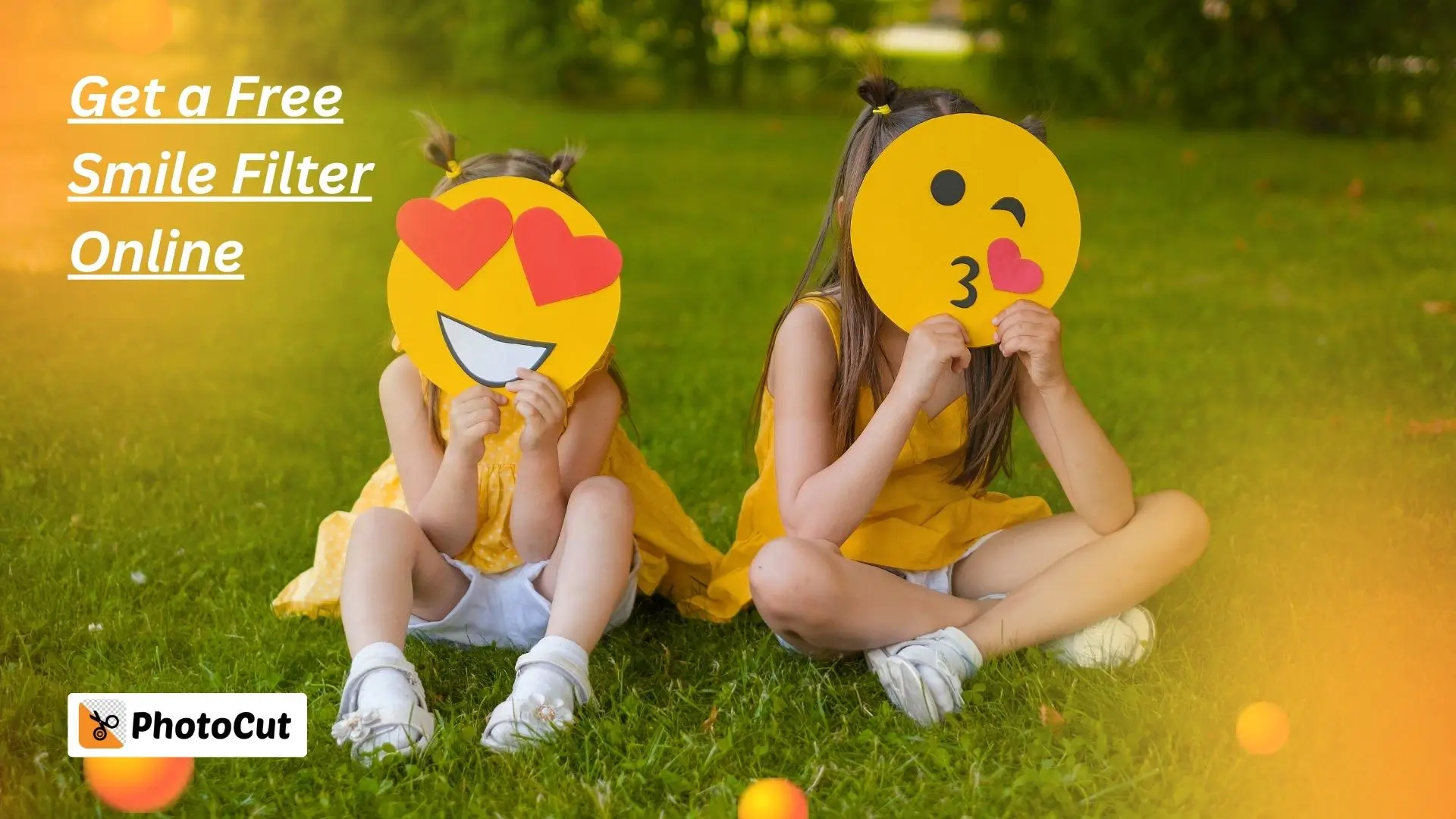 Two girls joyfully holding smiley face stickers while sitting on the grass, surrounded by a sunny outdoor setting.